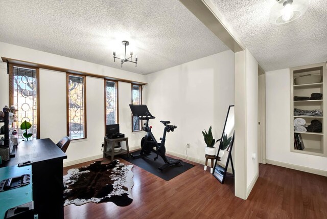 exercise room featuring a notable chandelier, built in features, a textured ceiling, and dark hardwood / wood-style flooring