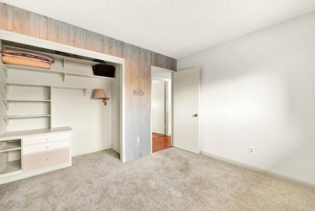 unfurnished bedroom with wooden walls, light colored carpet, a closet, and a textured ceiling