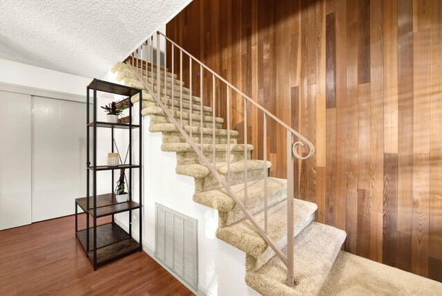 stairs with hardwood / wood-style flooring, a textured ceiling, and wood walls