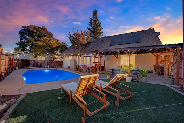 pool at dusk with an outdoor living space, a patio area, and a lawn