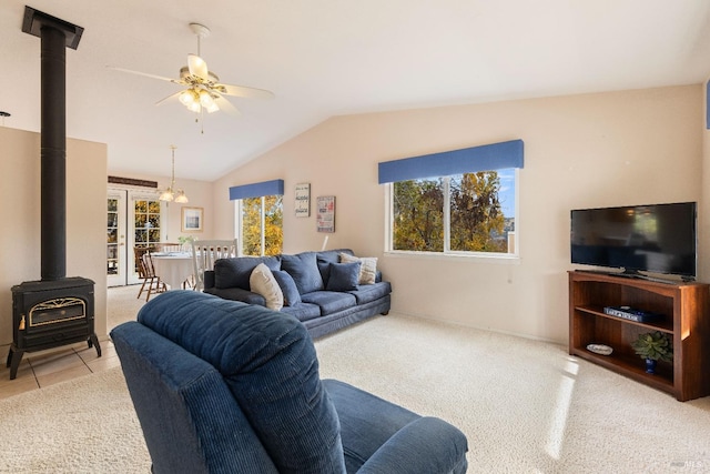 carpeted living room with ceiling fan with notable chandelier, a wood stove, a wealth of natural light, and lofted ceiling