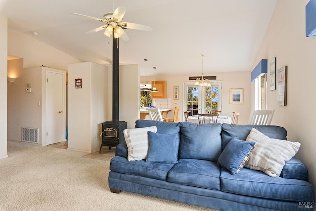 carpeted living room featuring a wood stove, ceiling fan with notable chandelier, and vaulted ceiling