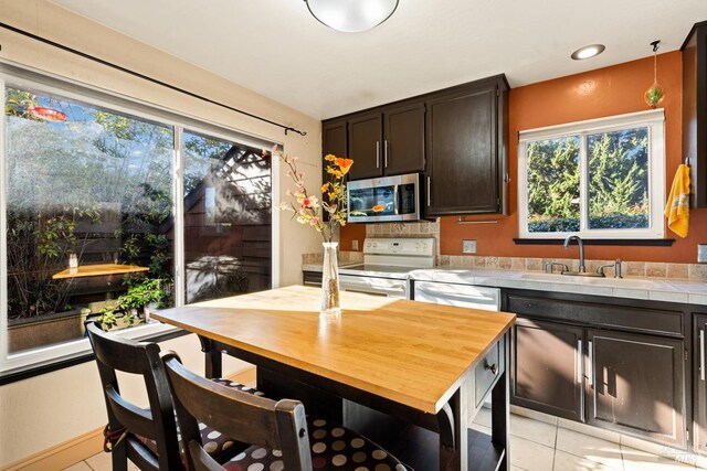 kitchen featuring light tile patterned flooring, sink, dark brown cabinets, appliances with stainless steel finishes, and plenty of natural light