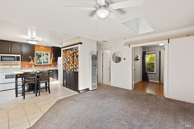 kitchen with white appliances, a skylight, light colored carpet, dark brown cabinets, and ceiling fan