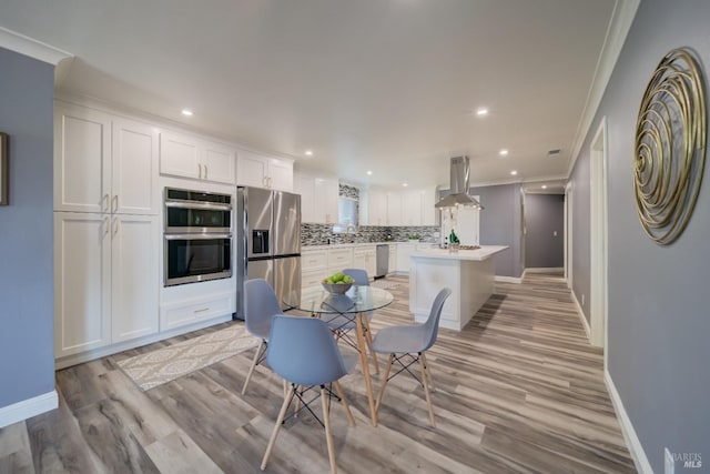 kitchen featuring a center island, white cabinets, wall chimney range hood, appliances with stainless steel finishes, and tasteful backsplash