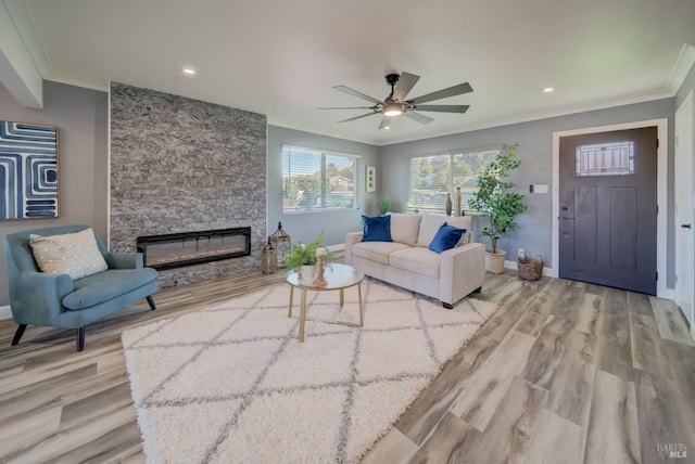 living room featuring light hardwood / wood-style floors, a stone fireplace, ceiling fan, and ornamental molding