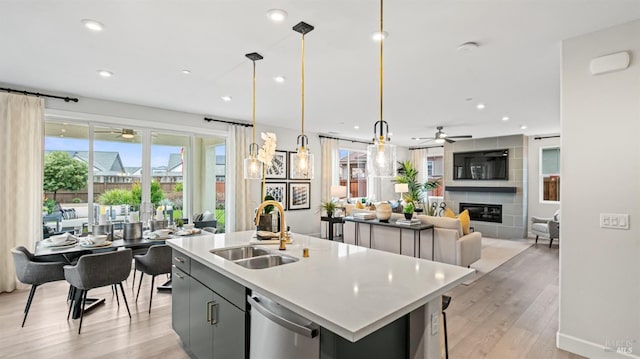 kitchen featuring a kitchen island with sink, a tile fireplace, sink, gray cabinets, and decorative light fixtures