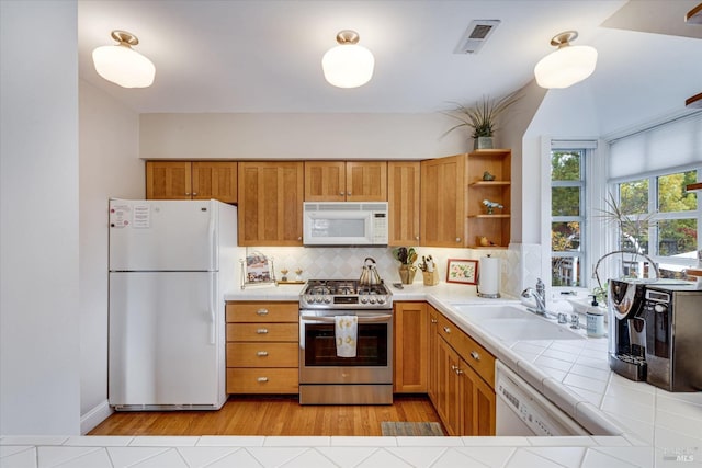 kitchen featuring white appliances, sink, light hardwood / wood-style flooring, decorative backsplash, and tile counters