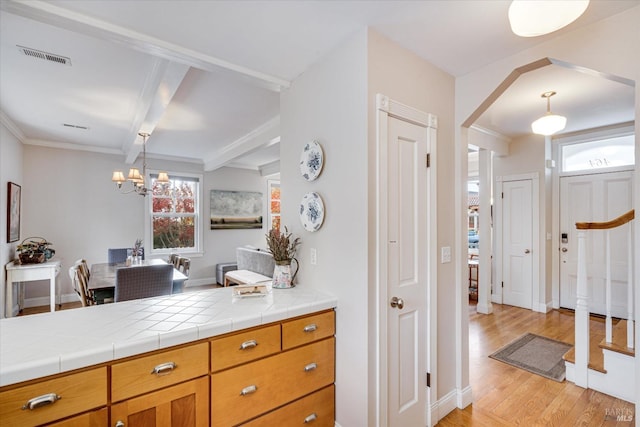 kitchen featuring light wood-type flooring, beam ceiling, tile countertops, a notable chandelier, and hanging light fixtures