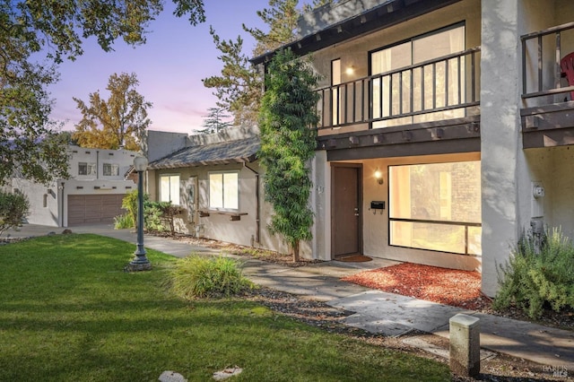 view of front of house featuring a garage, a lawn, and a balcony