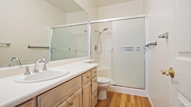 bathroom featuring vanity, wood finished floors, toilet, and a shower with door