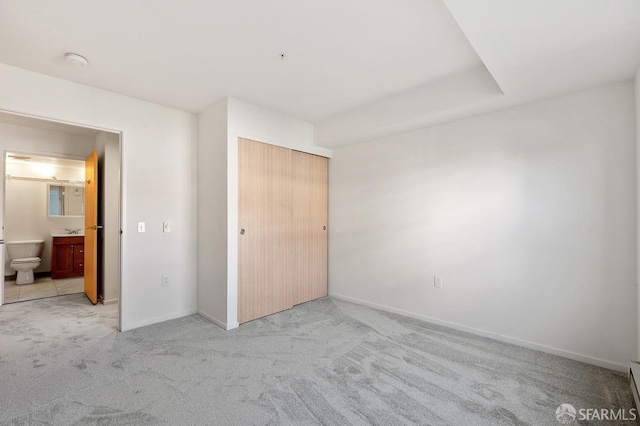 unfurnished bedroom featuring a baseboard radiator, light carpet, connected bathroom, and a closet