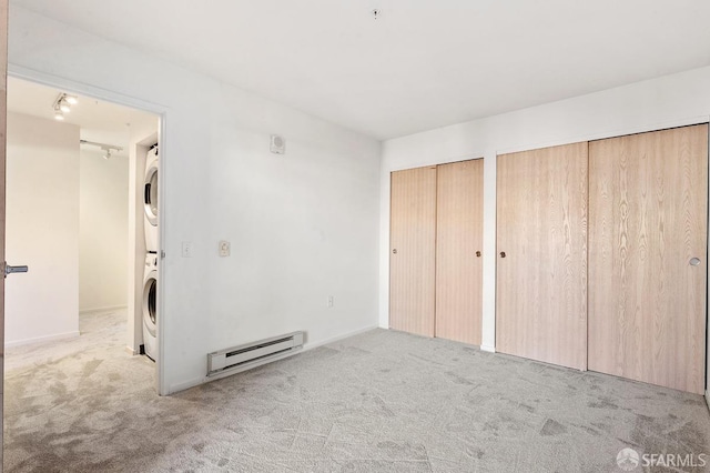 unfurnished bedroom with baseboard heating, stacked washer and dryer, light colored carpet, and two closets