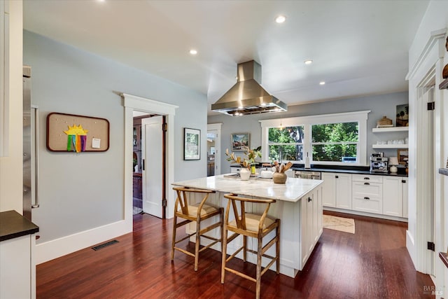 kitchen featuring white cabinets, a kitchen island, dark hardwood / wood-style flooring, dark stone countertops, and island range hood