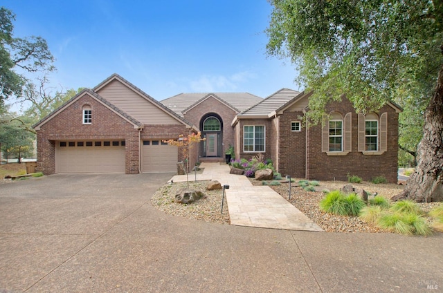 ranch-style house with driveway, brick siding, an attached garage, and a tiled roof