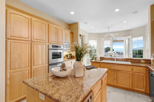 kitchen with light brown cabinets, a sink, a kitchen island, appliances with stainless steel finishes, and light stone countertops