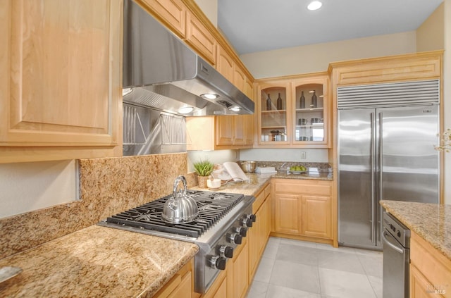 kitchen featuring under cabinet range hood, glass insert cabinets, light brown cabinets, and appliances with stainless steel finishes