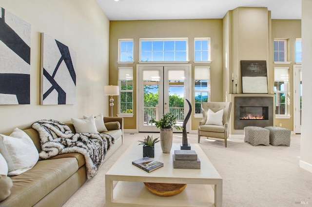 carpeted living area with a glass covered fireplace, a high ceiling, french doors, and baseboards