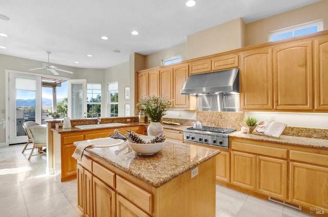 kitchen with a kitchen island, light stone countertops, under cabinet range hood, stainless steel gas stovetop, and a sink