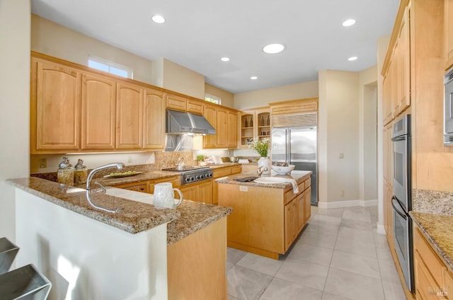 kitchen featuring under cabinet range hood, light stone counters, a center island, recessed lighting, and stainless steel appliances