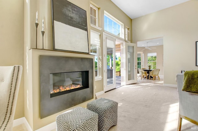 interior space with baseboards, carpet, french doors, a high ceiling, and a glass covered fireplace