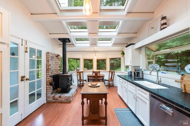 kitchen featuring a wood stove, sink, light hardwood / wood-style flooring, stainless steel dishwasher, and white cabinets