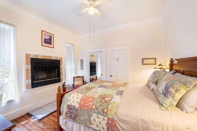 bedroom with a tile fireplace, ceiling fan, ornamental molding, and light wood-type flooring