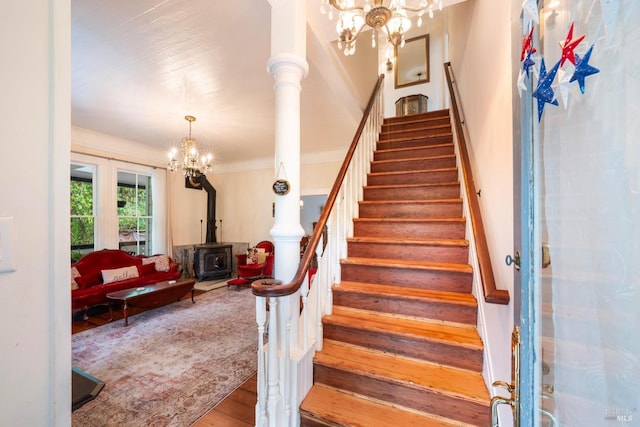 stairs featuring hardwood / wood-style floors, an inviting chandelier, a wood stove, and ornamental molding