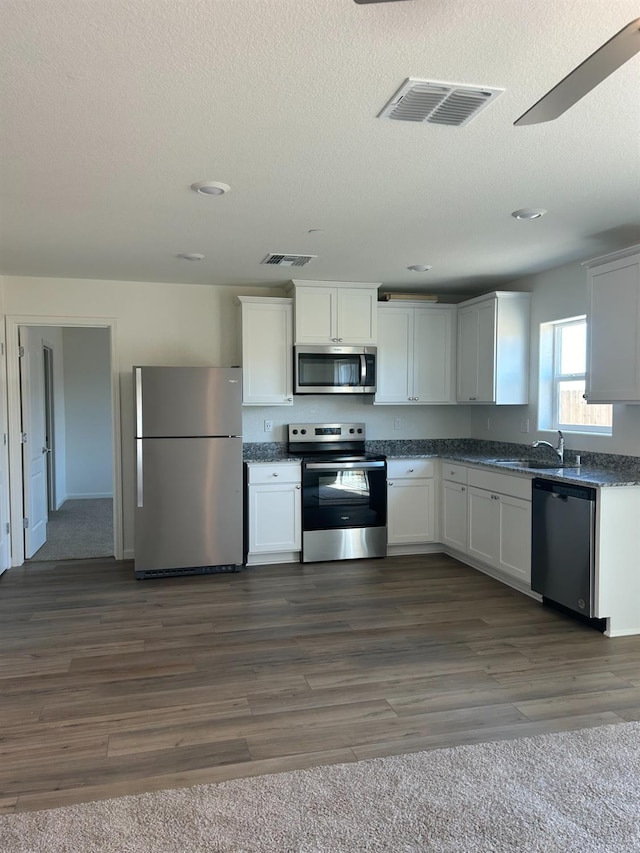 3060 Stones Ln, Stockton, CA 95212 - kitchen with appliances with stainless steel finishes, a textured ceiling, dark countertops, dark wood-style floors, and white cabinetry