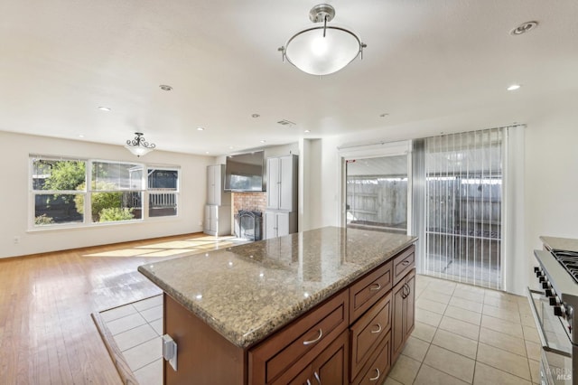 kitchen with light stone countertops, stainless steel gas stove, decorative backsplash, a kitchen island, and light wood-type flooring