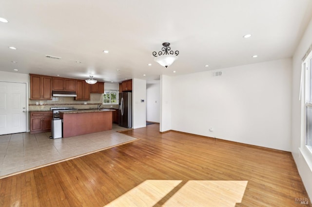 kitchen featuring a kitchen island with sink, light hardwood / wood-style flooring, decorative backsplash, decorative light fixtures, and stainless steel appliances