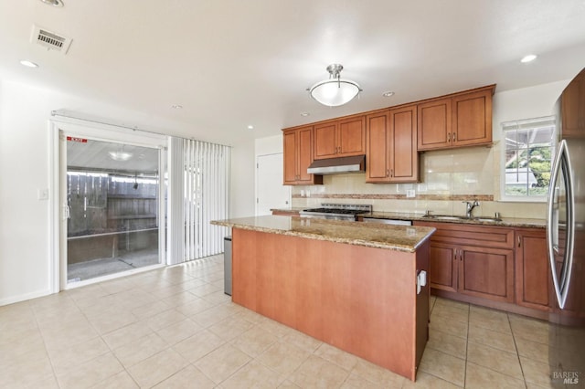 kitchen with light stone countertops, appliances with stainless steel finishes, decorative backsplash, sink, and a center island