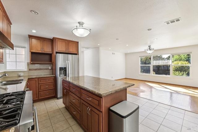 kitchen featuring appliances with stainless steel finishes, light wood-type flooring, light stone counters, sink, and a kitchen island