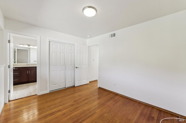 unfurnished bedroom featuring hardwood / wood-style flooring, ensuite bath, a closet, and sink