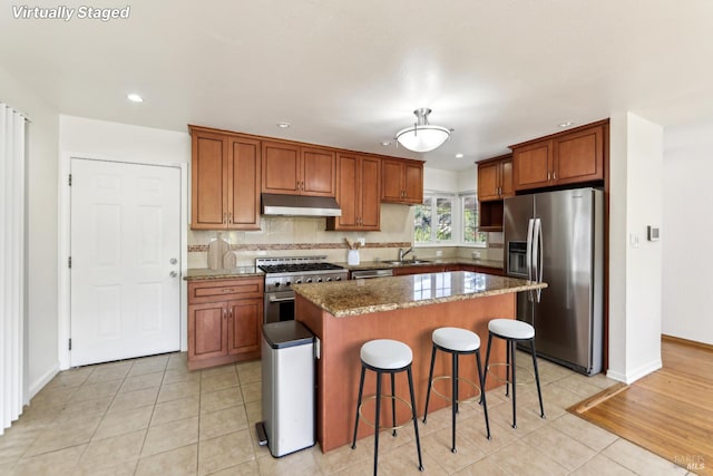 kitchen with a kitchen breakfast bar, sink, stone countertops, a kitchen island, and stainless steel appliances