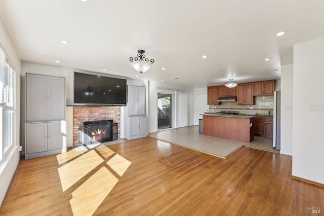 kitchen featuring refrigerator, tasteful backsplash, a brick fireplace, light hardwood / wood-style flooring, and a kitchen island