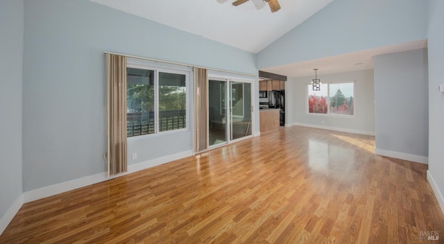 unfurnished living room featuring ceiling fan with notable chandelier, light wood-type flooring, and high vaulted ceiling