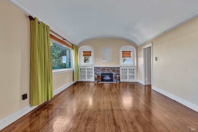 unfurnished living room featuring vaulted ceiling, a healthy amount of sunlight, a stone fireplace, and hardwood / wood-style floors