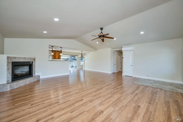 unfurnished living room featuring ceiling fan, vaulted ceiling, a tile fireplace, and light hardwood / wood-style flooring