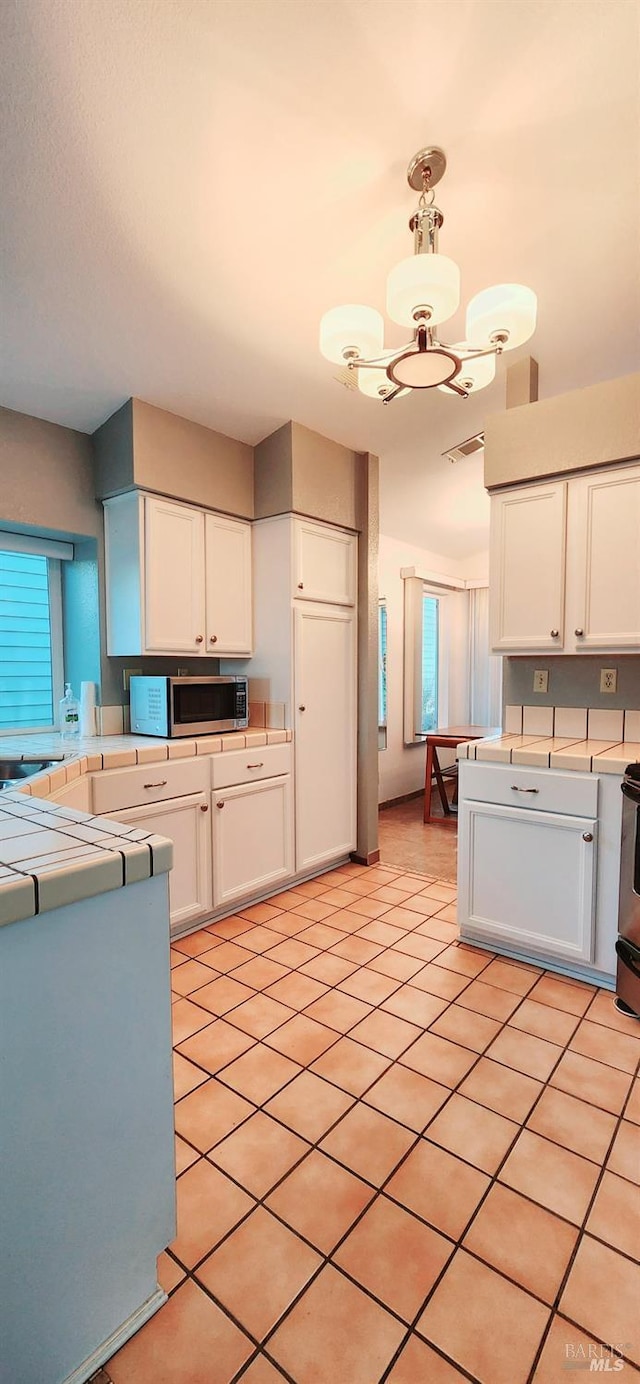 kitchen with white cabinets, light tile patterned floors, stainless steel appliances, and a chandelier