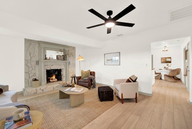 living room with a high end fireplace, visible vents, ceiling fan, and light wood finished floors