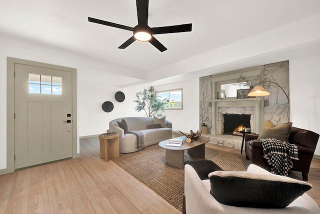 living room featuring baseboards, a fireplace, a ceiling fan, and wood finished floors