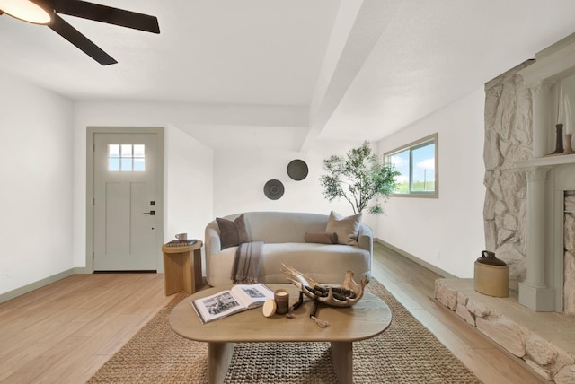 living room featuring baseboards, ceiling fan, a stone fireplace, and light wood finished floors