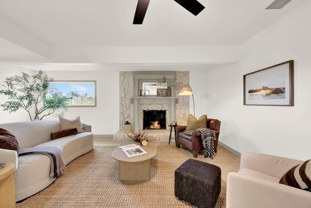 living room with ceiling fan, a premium fireplace, wood finished floors, visible vents, and baseboards