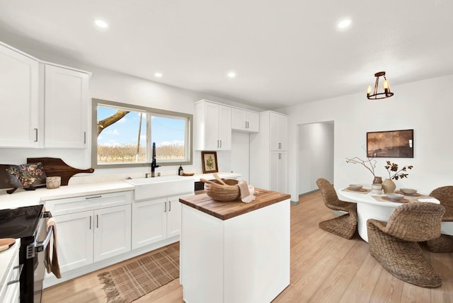 kitchen with black electric range, recessed lighting, light wood-style flooring, white cabinets, and a sink