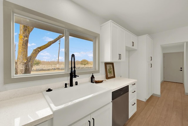 kitchen with stainless steel dishwasher, a sink, light wood-style flooring, and white cabinets