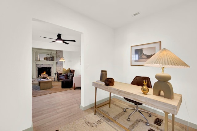 home office featuring ceiling fan, a premium fireplace, wood finished floors, visible vents, and baseboards