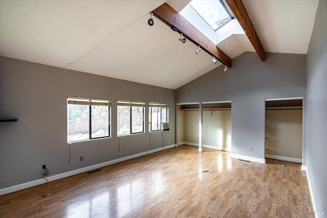 unfurnished bedroom featuring high vaulted ceiling, a skylight, beam ceiling, light hardwood / wood-style floors, and multiple closets