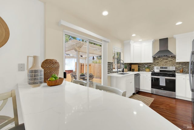 kitchen featuring white cabinets, wall chimney range hood, dark hardwood / wood-style floors, light stone countertops, and stainless steel appliances