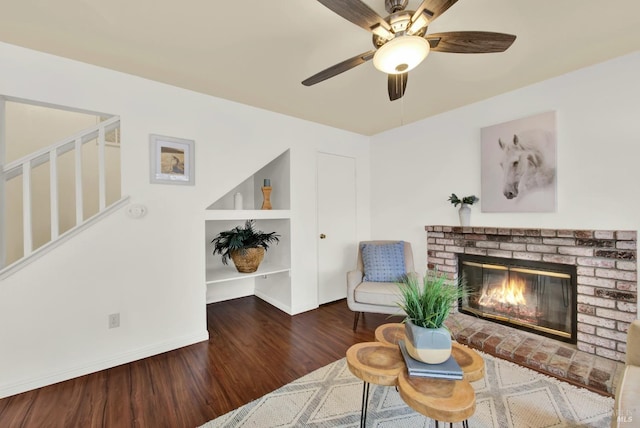 living area with dark hardwood / wood-style flooring, a brick fireplace, and ceiling fan